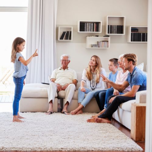 family sitting on the sofa together watching little girl standing up in living room