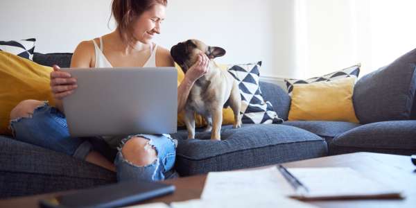 smiling woman on the sofa with her dog and n the computer