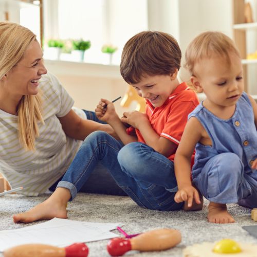 smiling mother and 2 sons playing with toys on the floor