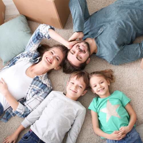 happy family laying on carpet with boxes around them after moving into their new home